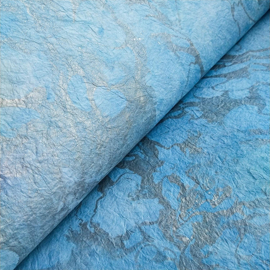 Close-up of Milano Kozo Paper - Design 2 by Kozo Studio, showcasing textured, crumpled mulberry paper with subtle silver marbling. The intricate patterns and folds create a dynamic surface with varying shades of blue and hints of metallic sheen.