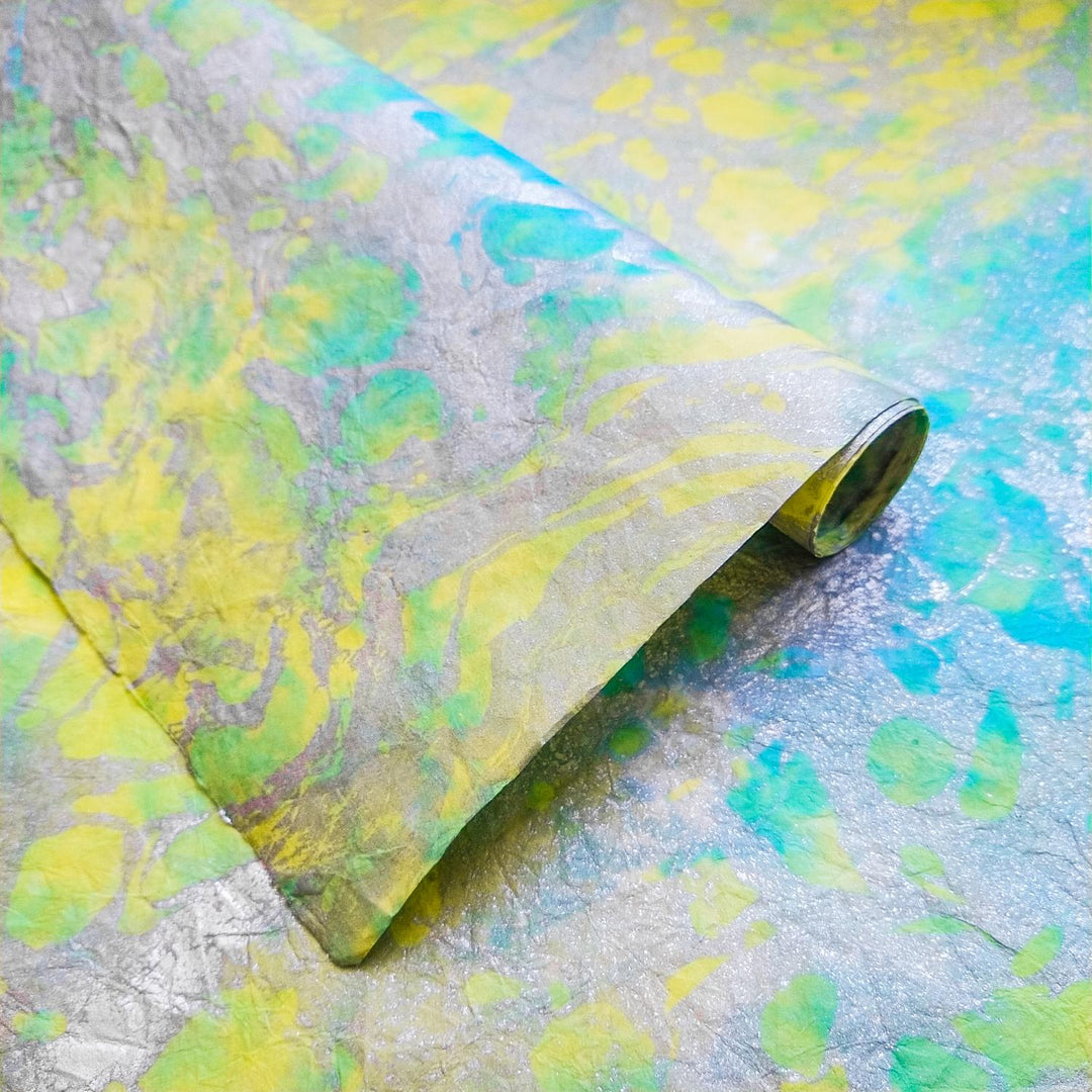 A close-up of Milano Kozo Paper - Design 3 by Kozo Studio highlights its crinkled texture and marbled pattern in vibrant shades of yellow, green, blue, and gray, forming an artistic abstract design.
