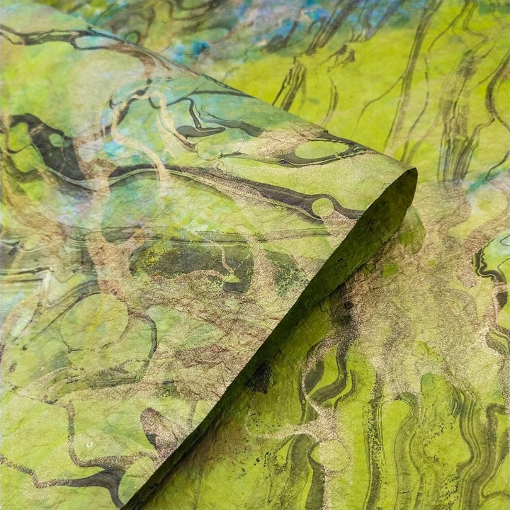 Close-up of Milano Kozo Paper - Design 5 by Kozo Studio, featuring textured, marbled mulberry paper with swirling patterns in green, black, and blue. The corner is slightly curled, showcasing its organic and fluid design.