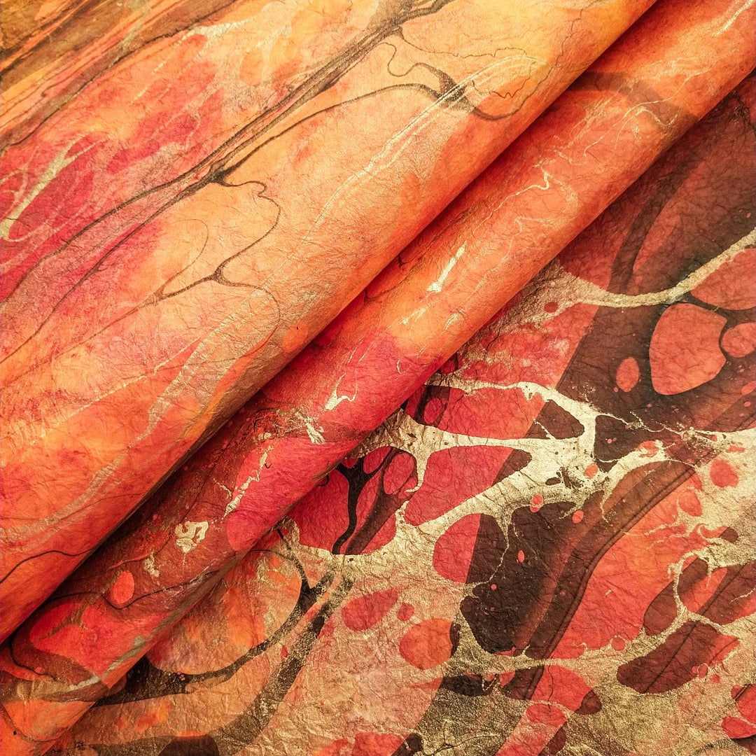 A vibrant sheet of handmade mulberry paper by Kozo Studio, featuring abstract orange, red, and yellow marbled swirls with black and silver accents, showcasing a fluid, textured design.