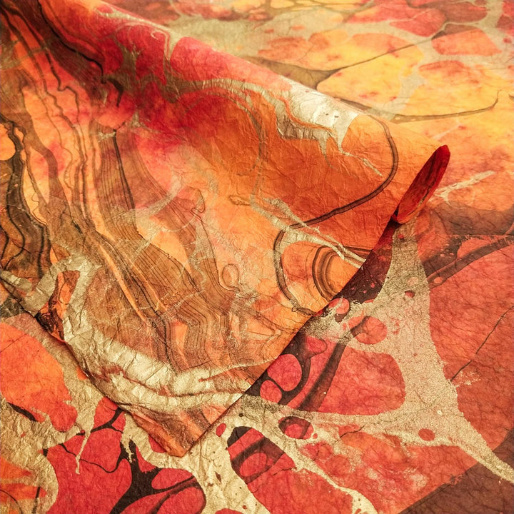 Close-up of Kozo Studio's handmade paper with swirling red, orange, and yellow patterns layered over textured mulberry paper and detailed with silver and black streaks.