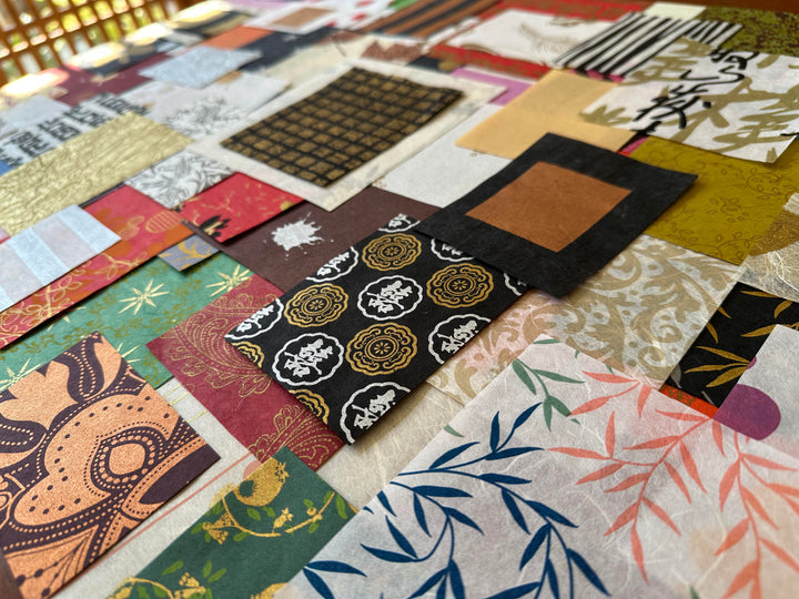 A vibrant patchwork quilt features the delicate texture and colorful patterns of the Kozo Studio Mulberry Paper Scrap Pack (100 Pieces) - Print Carnival, showcasing floral designs, geometric shapes, and text in shades of black, gold, red, and green.