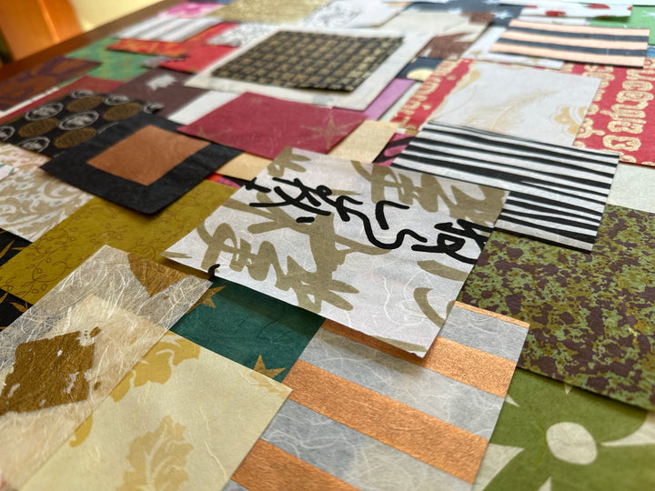 On a table, Kozo Studios Mulberry Paper Scrap Pack (100 Pieces) - Print Carnival showcases an array of textured paper squares featuring elegant Mulberry and delicate Rice Papers. The diverse patterns include stripes, floral motifs, and abstract designs in colors like gold, green, black, and red.