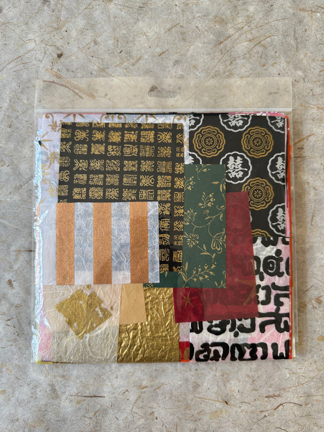 Kozo Studio handmade paper scrap pack includes 100 pieces of multicolored mulberry paper with gold, red, green, and black patterns.