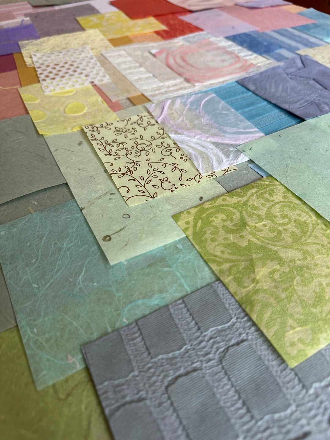 A close-up of Kozo Studios Mulberry Paper Scrap Pack (100 Pieces) - Spring Pastel, featuring a colorful patchwork of overlapping paper squares with diverse textures and patterns like florals, swirls, and geometric designs in pastel and vibrant hues.