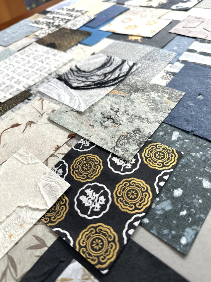 Artistic photo of Kozo Studio's mulberry paper variety pack. This handmade paper collection includes 100 unique scraps, offering endless creative possibilities in blue, white, and gold hues.