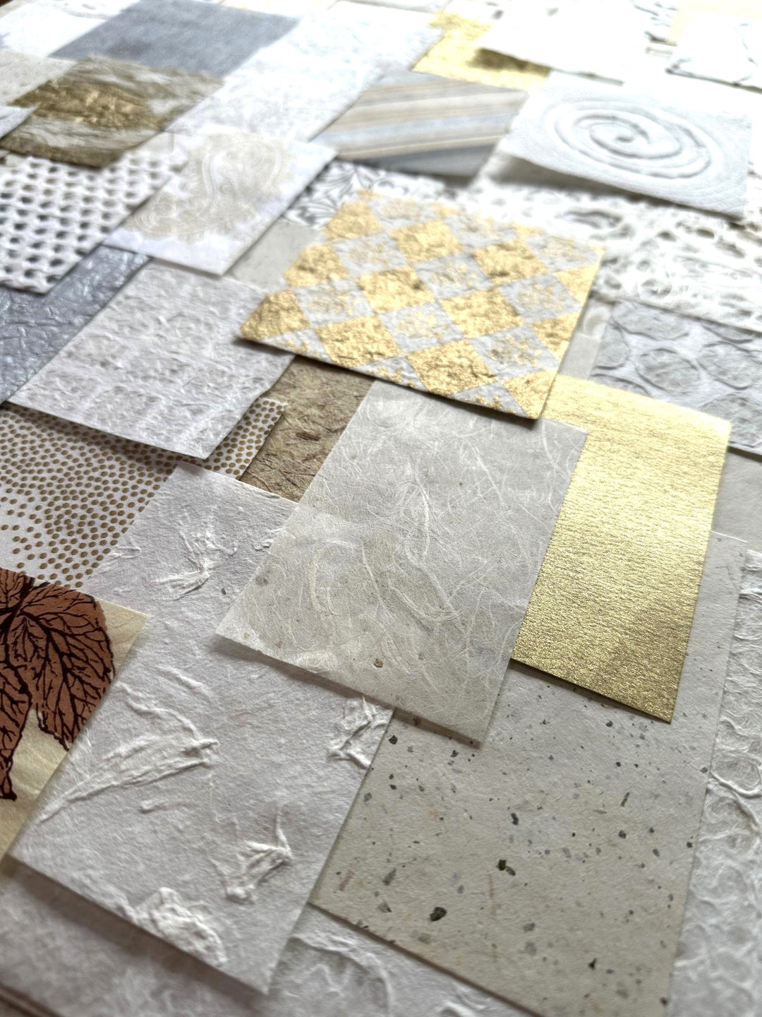 Close-up of a textured collage created from Kozo Studios Mulberry Paper Scrap Pack (100 Pieces) - Golden Harvest, featuring rice and mulberry papers in gold, white, and earthy tones. The design includes swirls, leaves, geometric shapes, and metallic sheen.