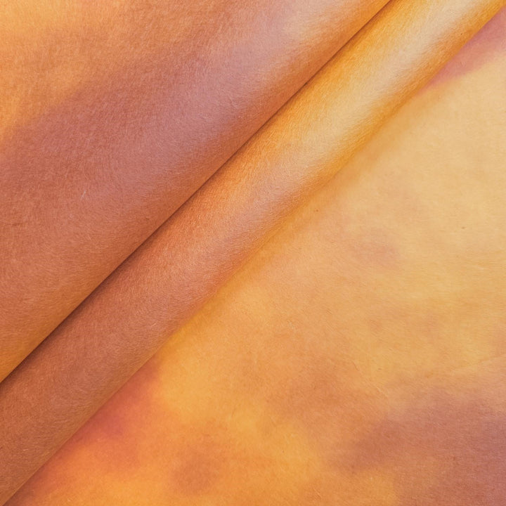 Close-up of two rolls of Ombre Kozo Paper (#7 Amber Dawn) by Kozo Studio, displaying warm shades of orange and brown. The smooth, slightly shiny texture showcases fine mulberry paper with a shimmering gradient effect across the surface.
