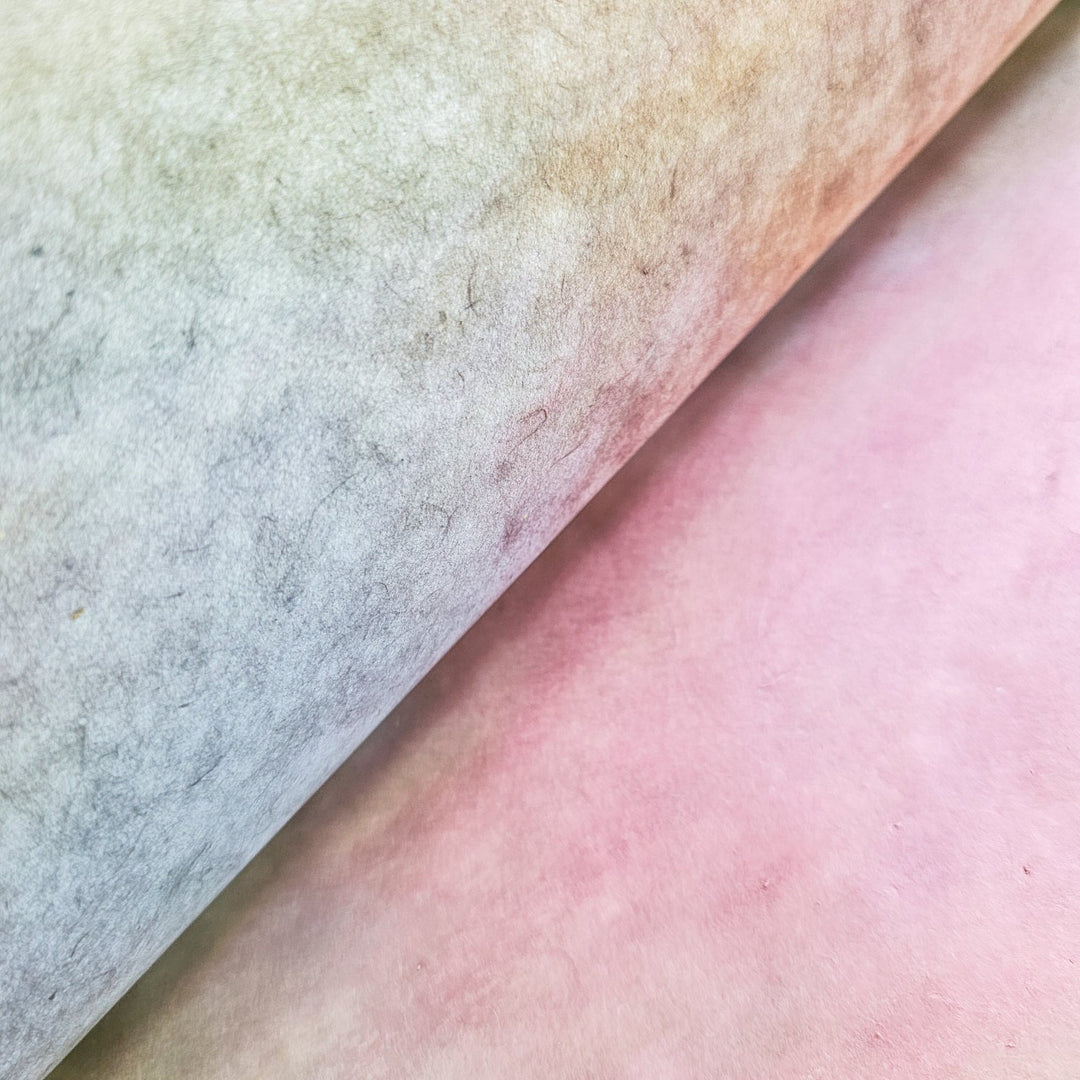 A close-up shows two overlapping sheets of Kozo Studios Ombre Kozo Paper (#4 Ethereal Rainbow) in pastel hues. The left mulberry sheet fades from light gray to green, and the right from soft pink to peach,.