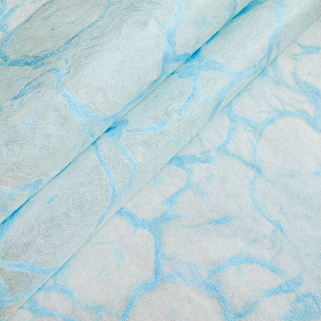 Blue marbled design on white mulberry paper by Kozo Studio, captured in a close-up of their Ripple Kozo handmade paper collection.