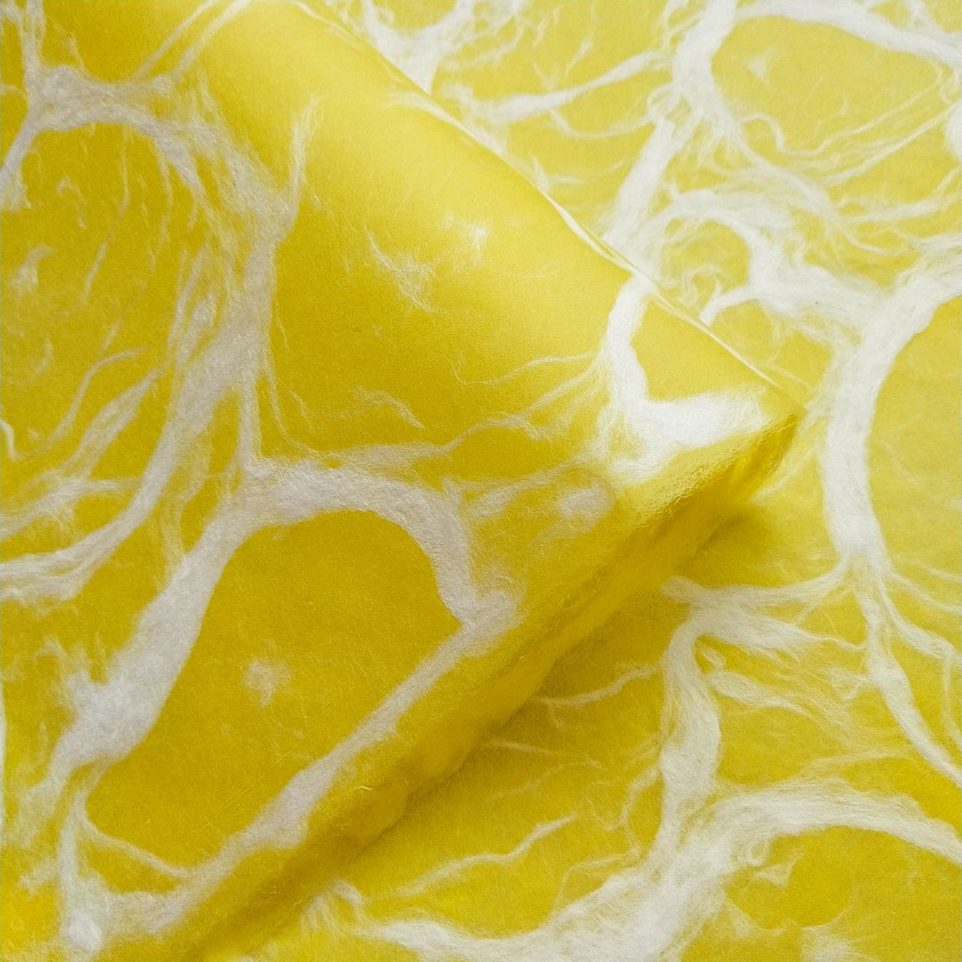 Close-up of Kozo Studio handmade paper featuring Ripple Kozo design with white fibrous swirls on textured yellow mulberry paper.