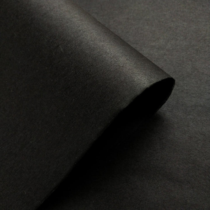 A macro shot of handmade paper from Kozo Studio in solid black, showcasing the fine texture of mulberry paper.