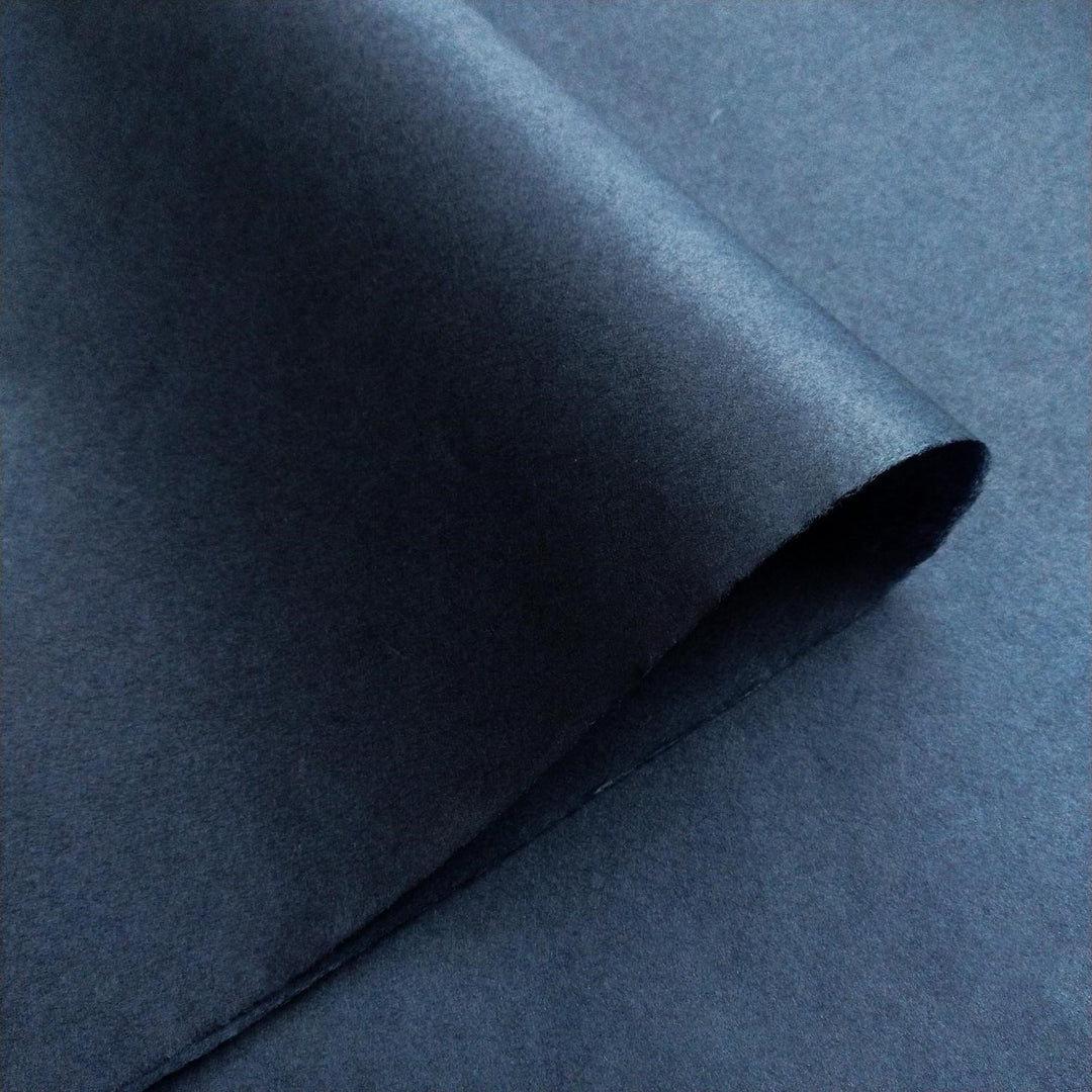 Textured surface of Kozo Studio handmade mulberry paper in denim blue, enhanced by soft light and shadow.