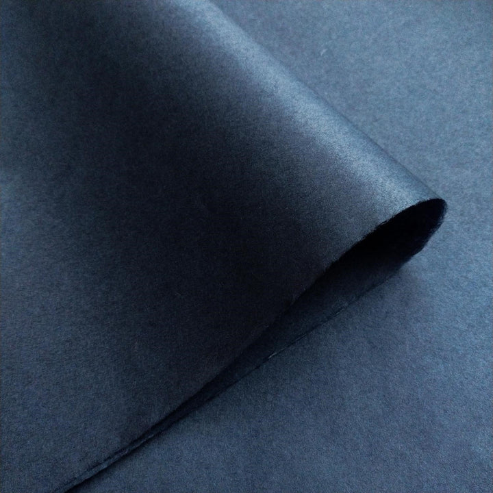Textured surface of Kozo Studio handmade mulberry paper in denim blue, enhanced by soft light and shadow.