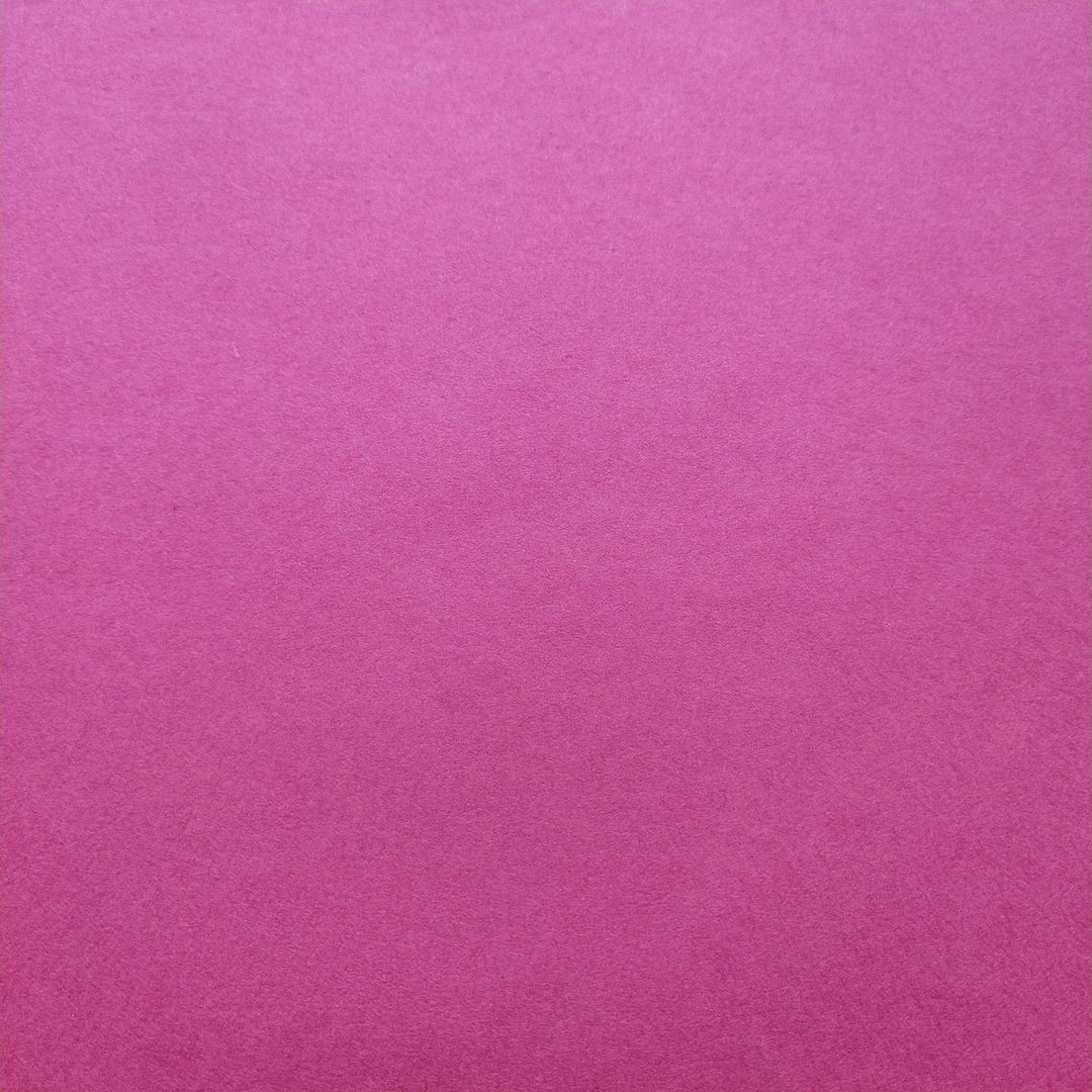 Handmade paper in a bold fuchsia hue from Kozo Studio, with a curled corner revealing the smooth surface and depth of mulberry fiber texture.
