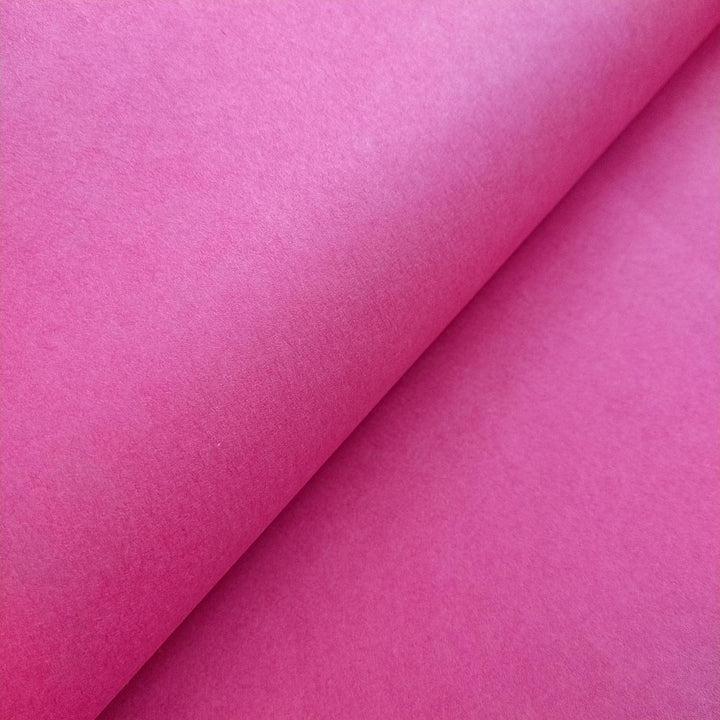 Textured surface of fuchsia handmade paper from Kozo Studio, with a rolled edge revealing the layered gradient and fibrous mulberry paper structure.