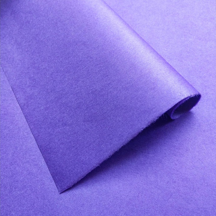 A roll of Kozo Studios Solid-Colored Kozo Paper in rich purple is partially unrolled against a matching background, showcasing a smooth, matte texture of mulberry paper.