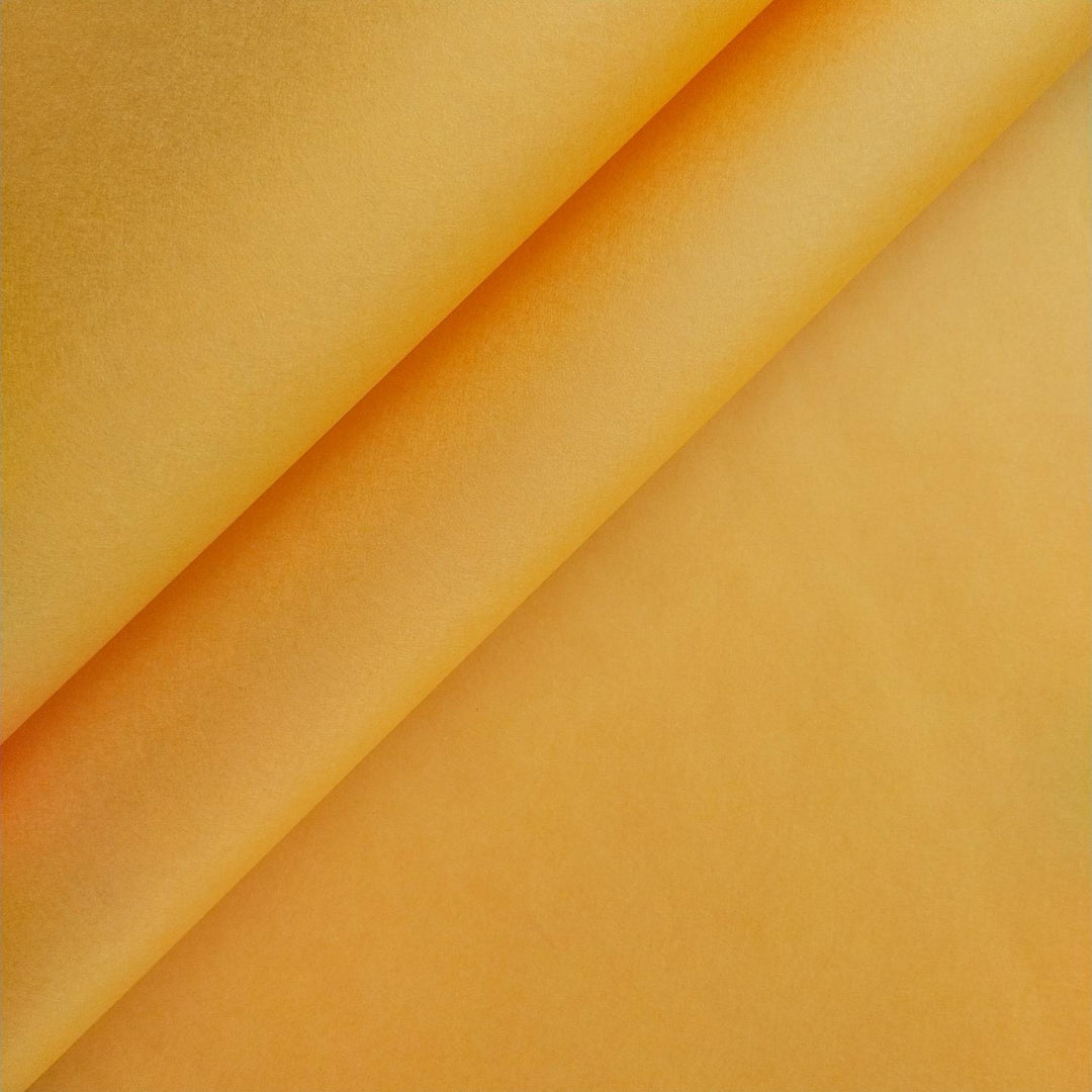 Close-up of saffron-colored mulberry paper by Kozo Studio showcasing its handmade texture, soft shadowing, and subtle color gradients across folded diagonal edges.