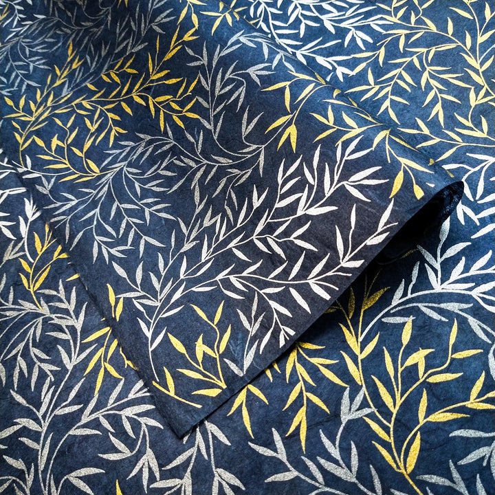 Intricately patterned Kozo Studio handmade paper featuring metallic leafy branches on deep blue, echoing the texture and movement of traditional mulberry paper.