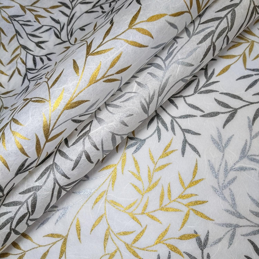 Close-up of handmade mulberry paper by Kozo Studio with metallic gold and silver leaf patterns screen-printed on a smooth white surface.