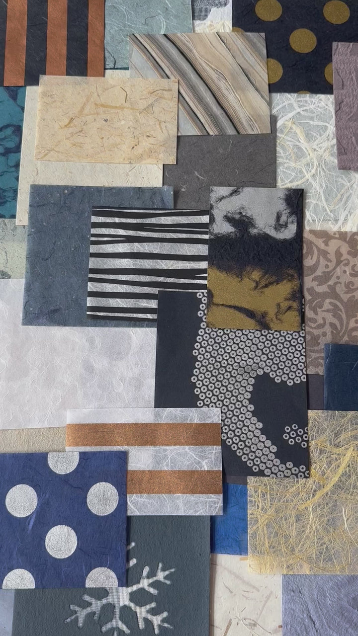 Close-up of assorted handmade mulberry paper pieces from Kozo Studio, featuring a variety of textures and colors in blue, white, and gold, ideal for collage or paper mache art.