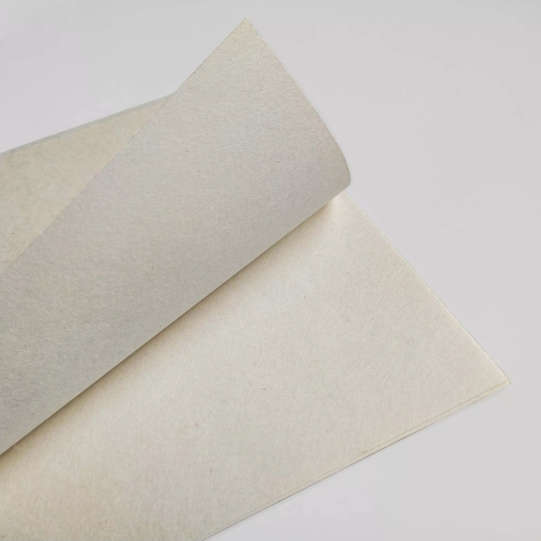 Close-up of a slightly curved sheet of A4 Extra Thin Natural Kozo Paper from Kozo Studio, 35 gsm. Its off-white with texture and features a visible crease where one corner slightly folds upward against a neutral background.