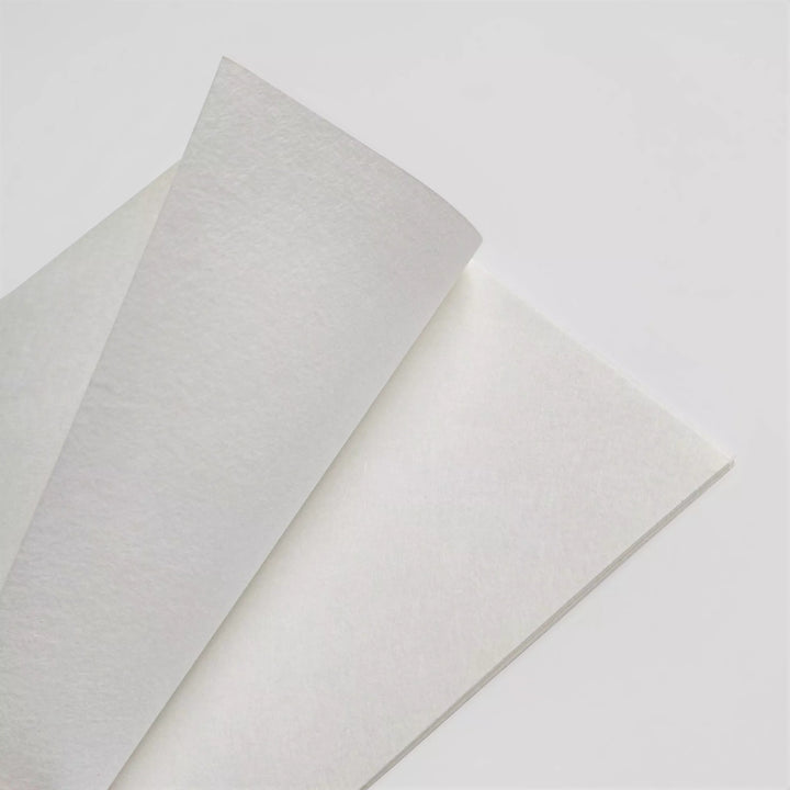 Two sheets of A4 White Kozo Paper from Kozo Studio partially overlap on a smooth, light gray background. The off-white papers soft appearance creates subtle shadows at the intersection, highlighting its texture and gentle curvature.