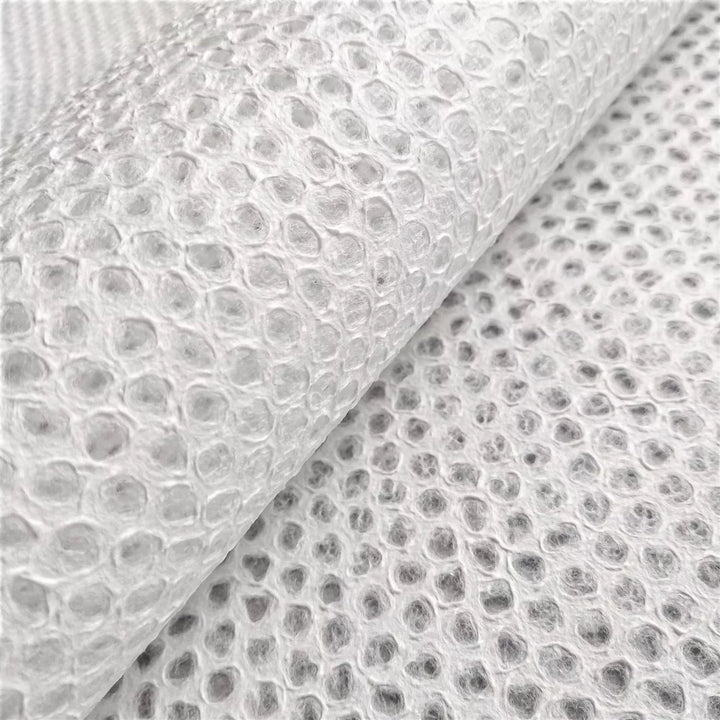 A roll of Handmade Lace Kozo Paper (Mini Dot) by Kozo Studio reveals a surface of rice paper, featuring evenly spaced mini dots. Overlapping sheets create an intriguing interplay of texture.