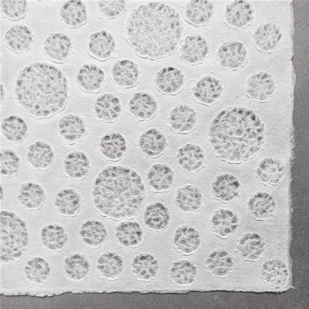 Handmade Lace Kozo Paper (Bubble) by Kozo Studio features textured white mulberry paper with embossed circular patterns, set against a plain gray background that highlights the intricate raised details.