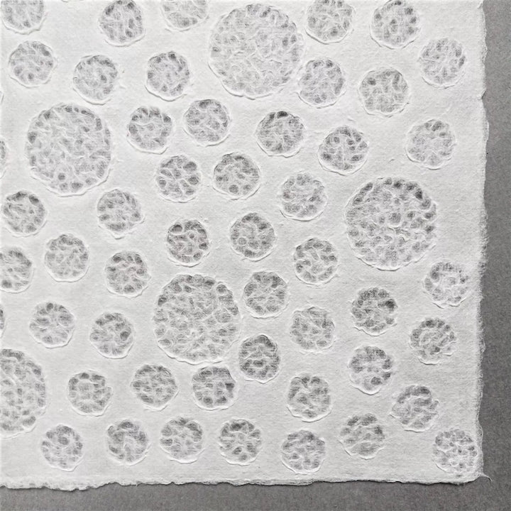 Handmade Lace Kozo Paper (Bubble) by Kozo Studio features textured white mulberry paper with embossed circular patterns, set against a plain gray background that highlights the intricate raised details.