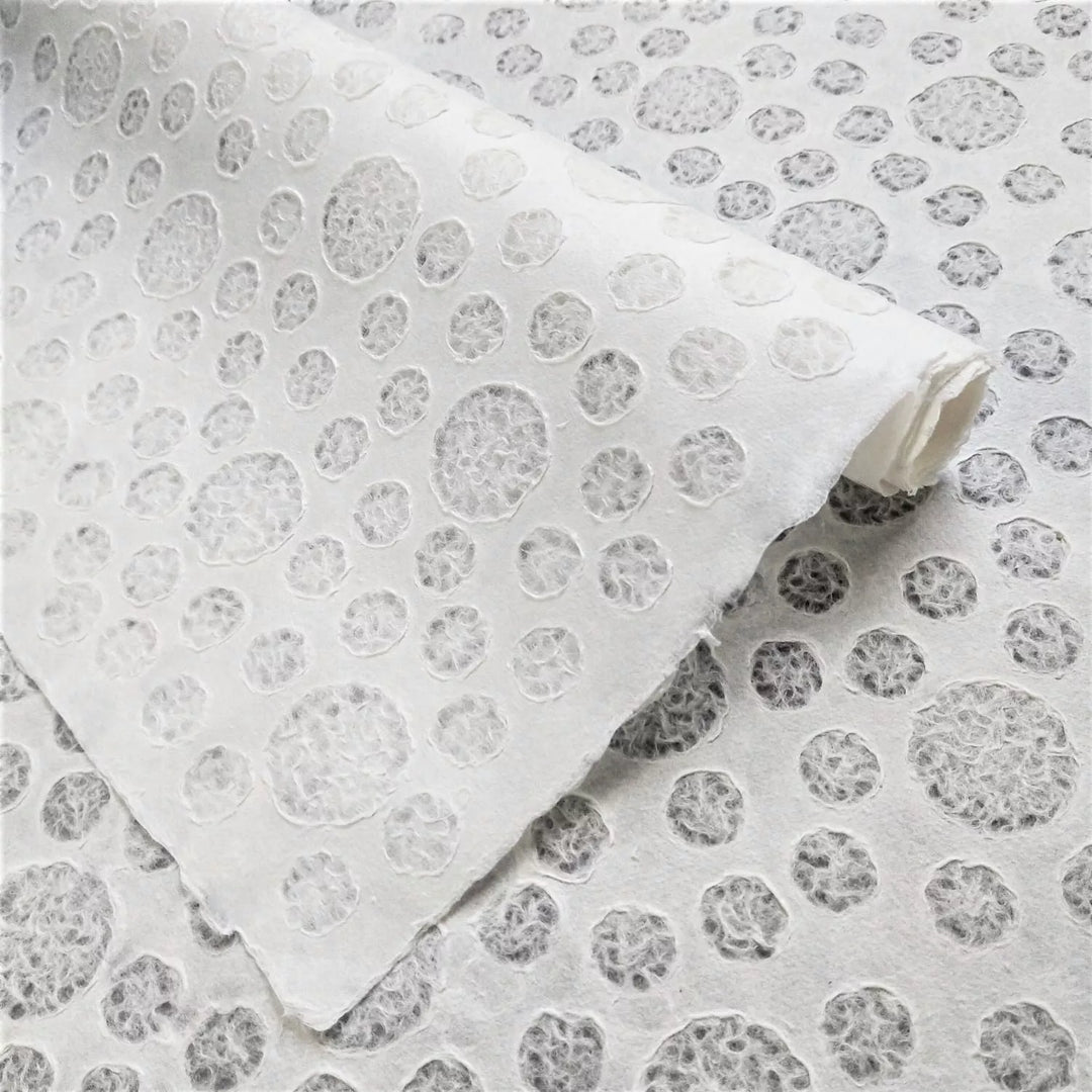 The Handmade Lace Kozo Paper (Bubble) by Kozo Studio is textured mulberry paper with a circular perforation pattern. It is partially folded, revealing a consistent design across the surface beneath.