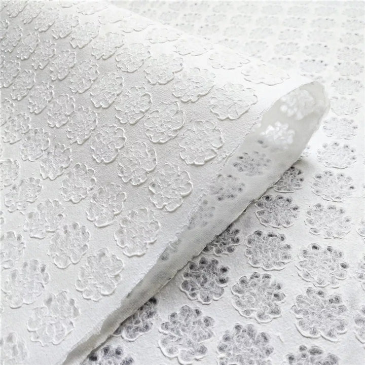 Close-up of Handmade Lace Kozo Paper (Floret) by Kozo Studio, featuring an embossed floral pattern similar to delicate rice paper. Raised flower-like shapes are evenly distributed, with a slight fold in the upper left corner that enhances its texture and detail.