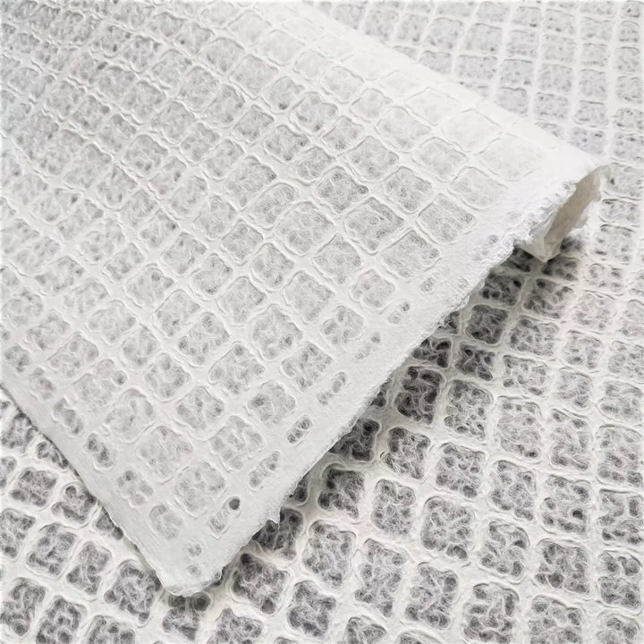 Close-up of delicate handmade paper from Kozo Studio, showcasing a waffle-textured sheet made from fine mulberry paper, perfect for lampshades and creative design projects.