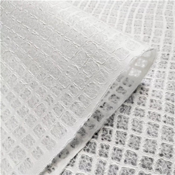 Translucent lace mulberry paper by Kozo Studio, photographed in close-up to reveal its intricate handmade waffle texture, used in fine craft and lighting design.