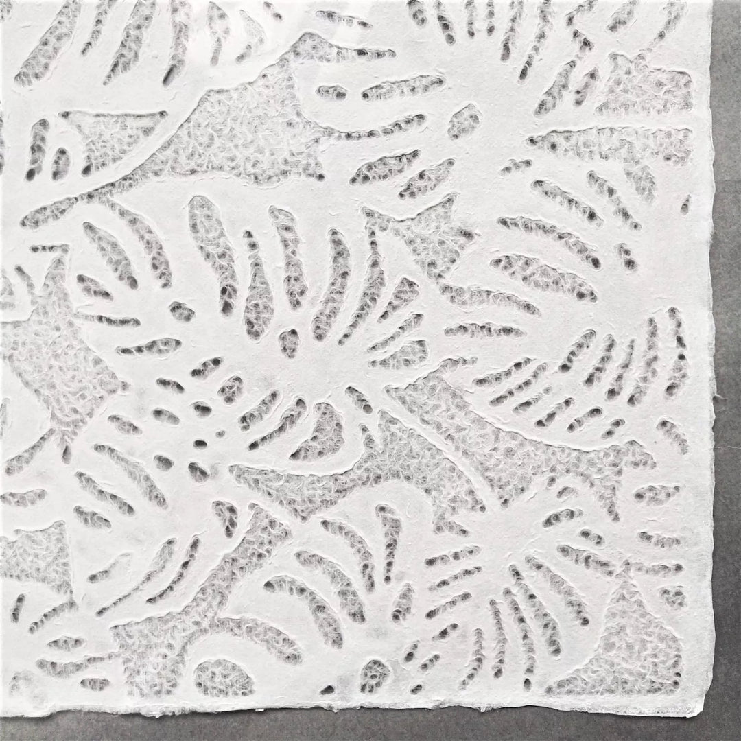 Detailed image of Kozo Studio handmade paper with Monstera-style lacework, rolled slightly to reveal the fine mulberry paper structure and its natural translucency.