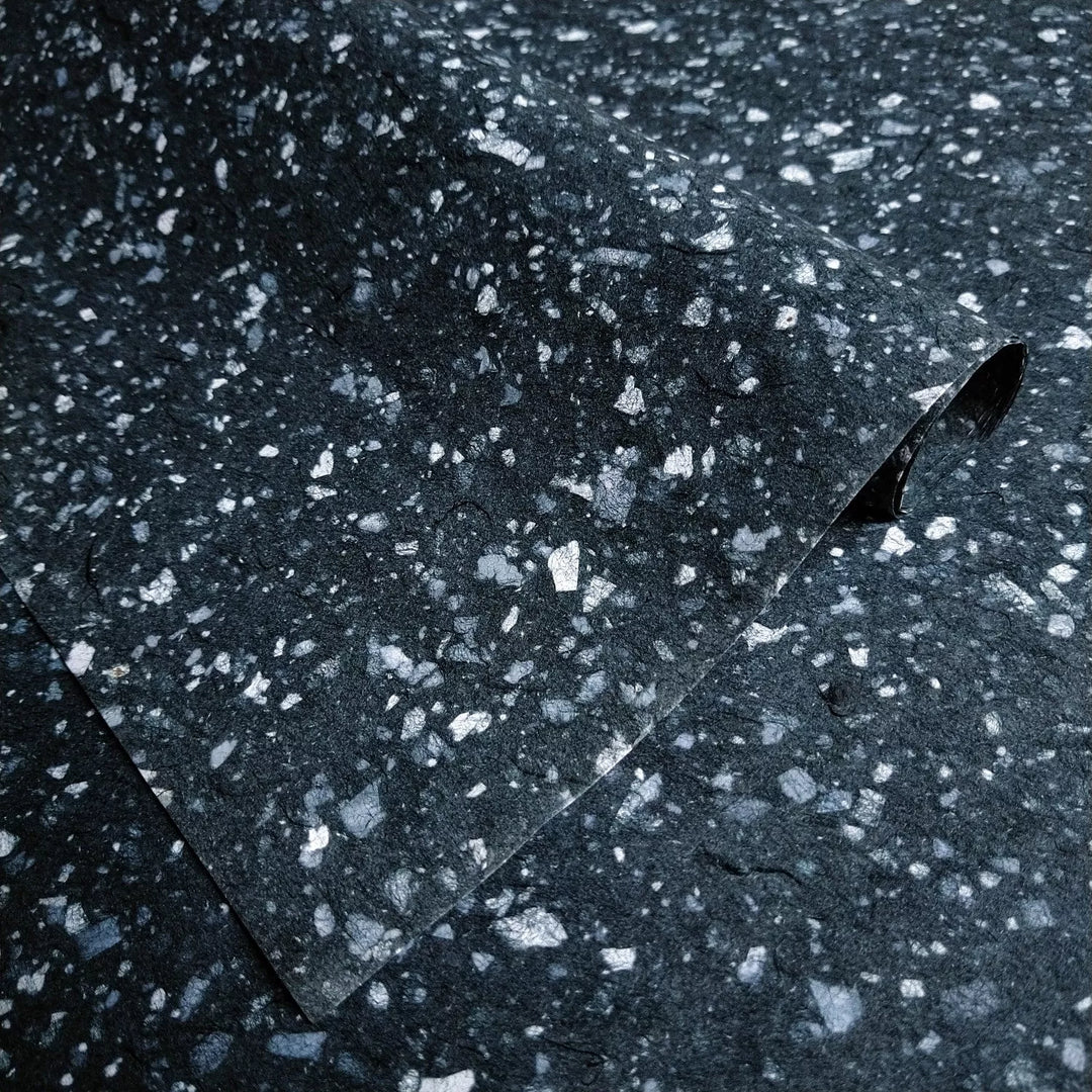 Handmade paper from Kozo Studio featuring white bond paper fragments over rich black mulberry pulp, creating a speckled granite-like texture ideal for art and craft projects.