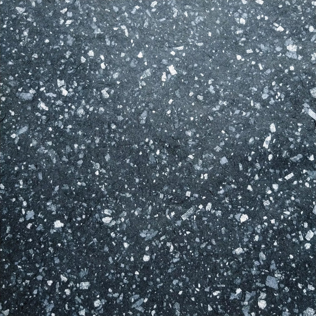 Speckled handmade paper crafted at Kozo Studio using white bond scraps on black mulberry pulp, offering flexibility and elegance for creative projects.