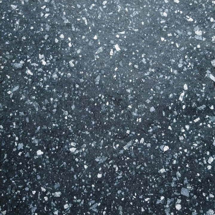 Speckled handmade paper crafted at Kozo Studio using white bond scraps on black mulberry pulp, offering flexibility and elegance for creative projects.