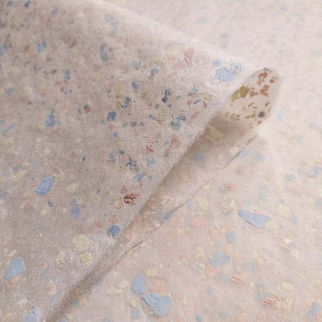 Close-up of speckled handmade paper created at Kozo Studio with pastel paper pieces embedded in creamy kozo mulberry pulp.