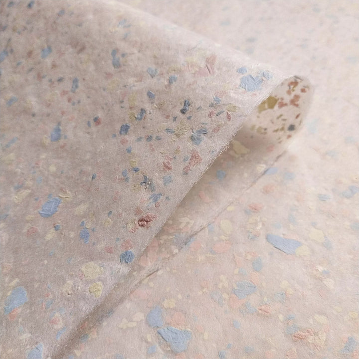 Close-up of speckled handmade paper created at Kozo Studio with pastel paper pieces embedded in creamy kozo mulberry pulp.