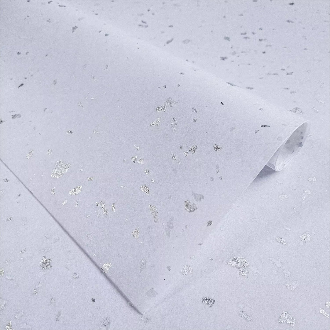 Bright white handmade mulberry paper with shiny silver flakes displayed elegantly at Kozo Studio, perfect for unique art and craft projects.