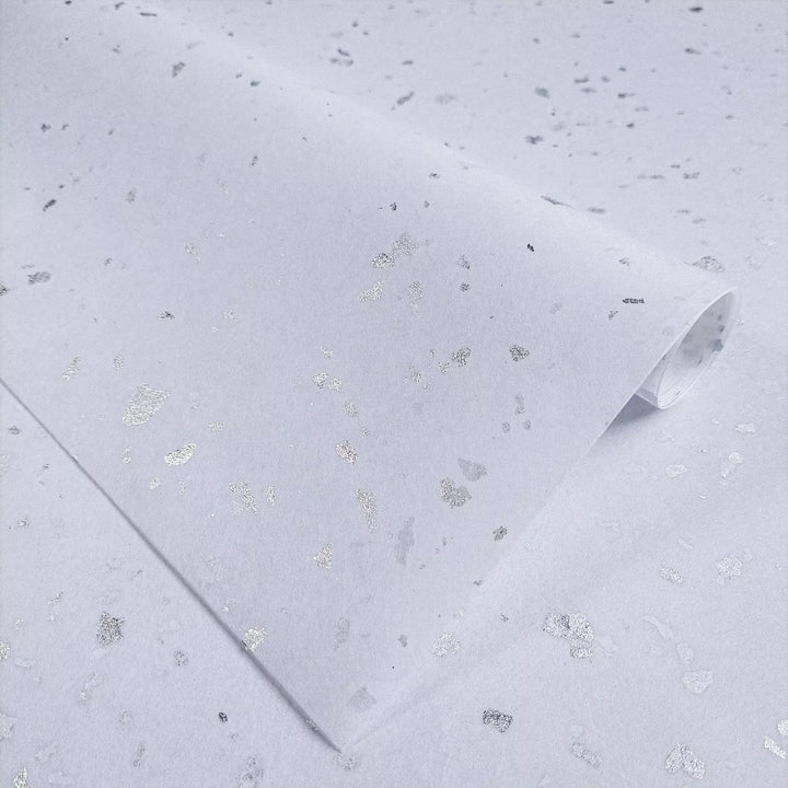 Bright white handmade mulberry paper with shiny silver flakes displayed elegantly at Kozo Studio, perfect for unique art and craft projects.