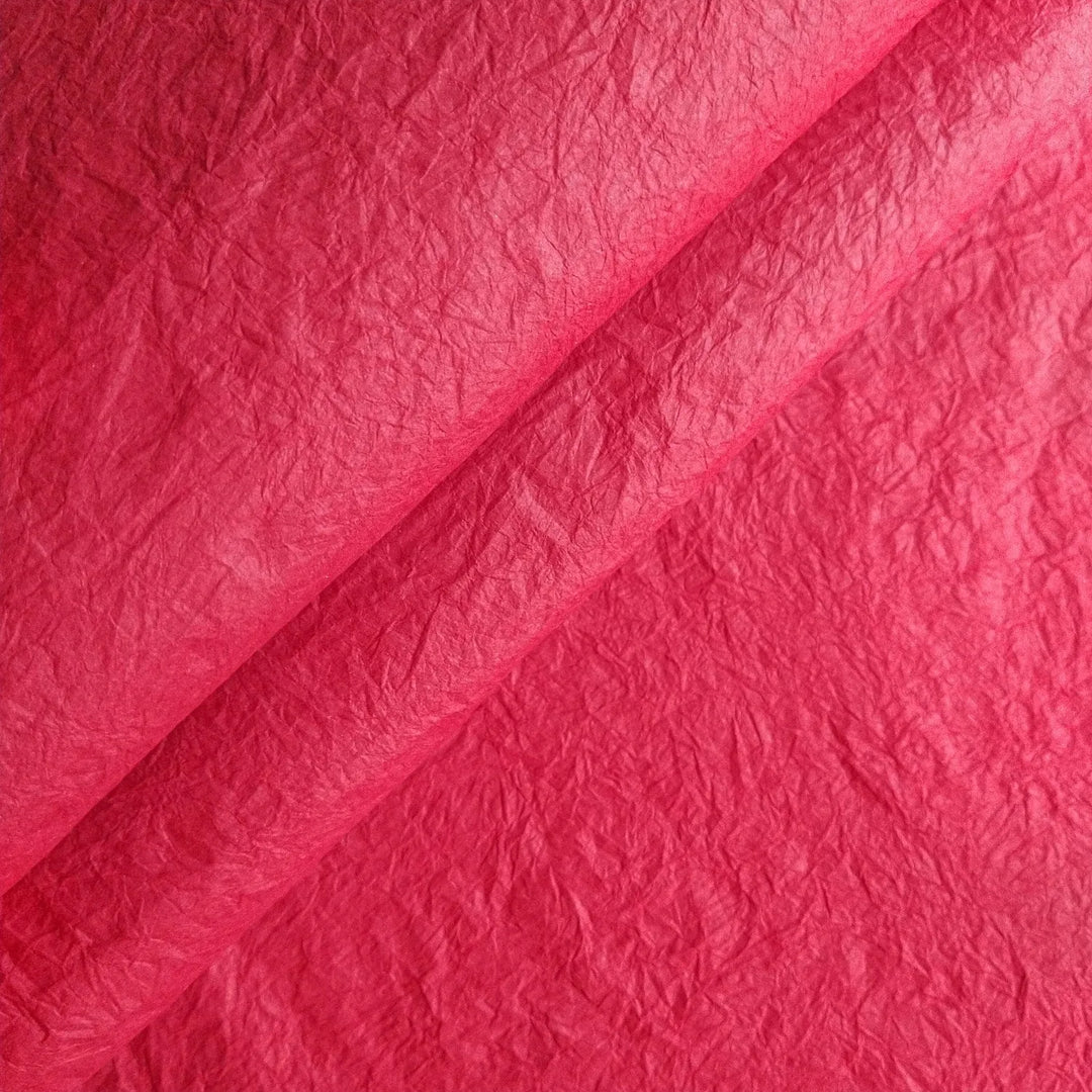A close-up of Kozo Studios Momigami Color Kozo Paper (Red) displays its crinkled and slightly folded surface. The lighting enhances the shades and texture, adding depth to its vibrant red color.