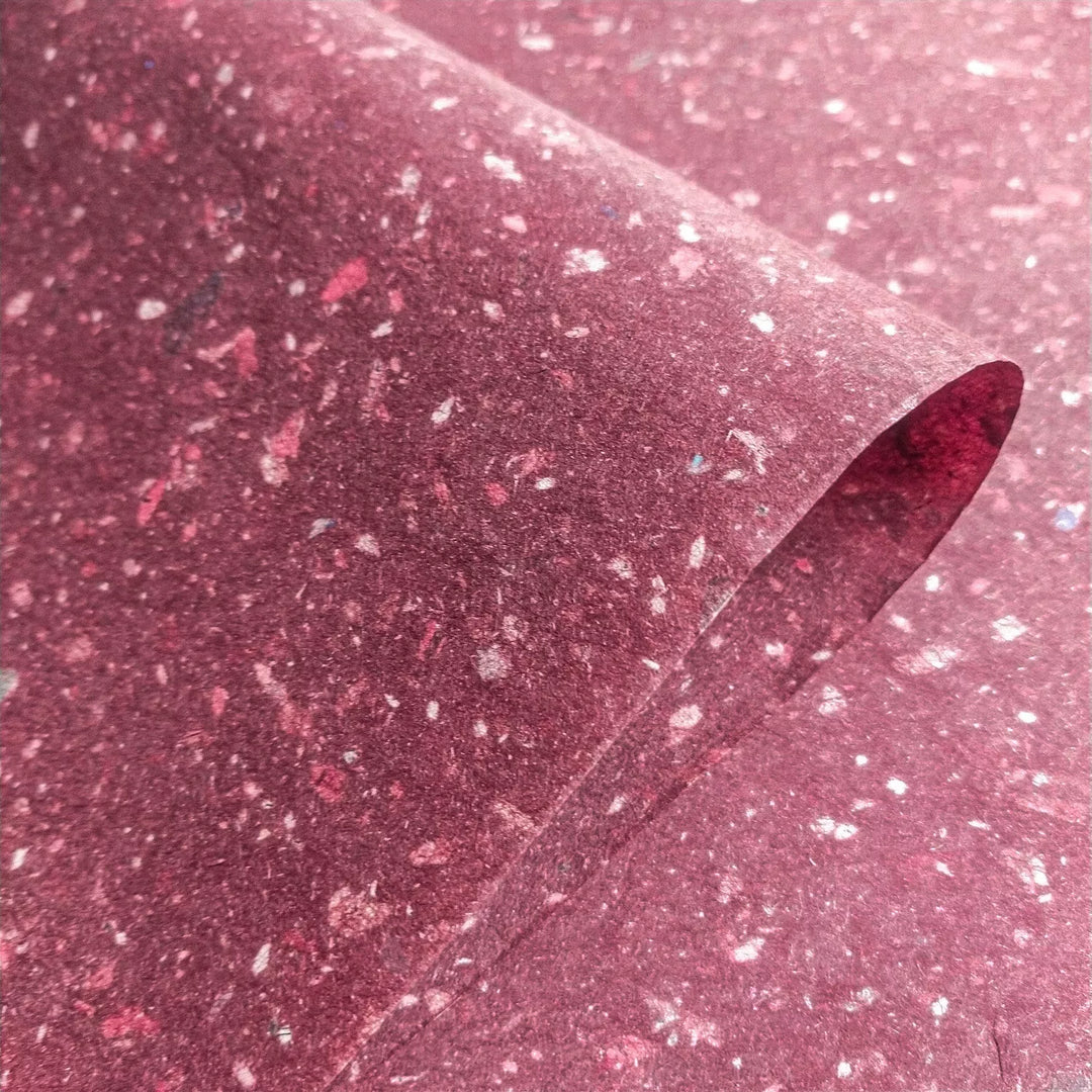 Close-up of speckled handmade paper from Kozo Studio. Made with kozo pulp and bits of newspaper, this flexible mulberry paper suits various sustainable craft applications.