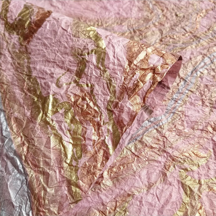 Close-up of crumpled Milano Kozo Paper - Design 15 (Pink) by Kozo Studio, featuring an uneven texture with pink and gold abstract patterns. Visible folds and creases add a tactile quality to the image.