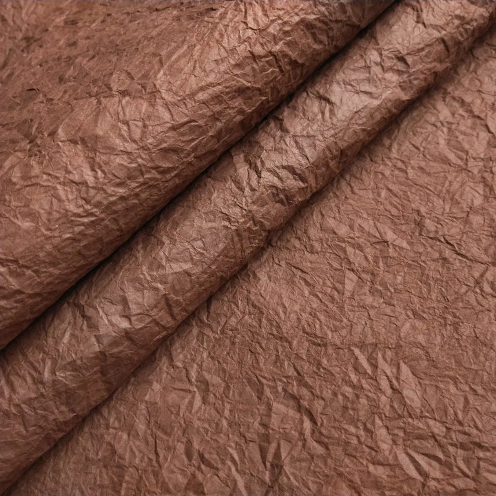 A close-up of Momigami Color Kozo Paper (Brown) by Kozo Studio reveals its crinkled surface with textured folds and wrinkles. The lighting accentuates the uneven texture, imparting a natural, rugged look.