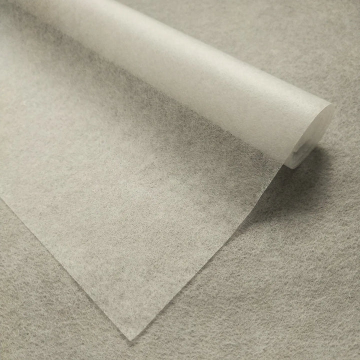 A close-up of Kozo Studios Conservator No.1 (8.5 gsm; 15 sheets/pack) washi paper unrolling onto a flat surface, highlighting its thin, translucent texture and smooth, slightly matte finish.