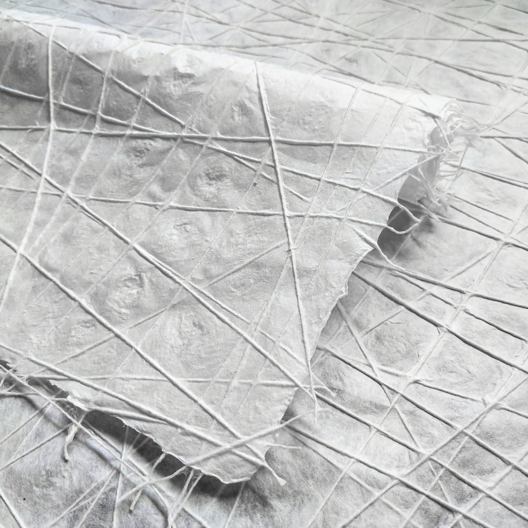 White handmade paper from Kozo Studio featuring interlaced cotton threads across mulberry pulp, showcasing an intricate, handcrafted texture with water dimpling details.