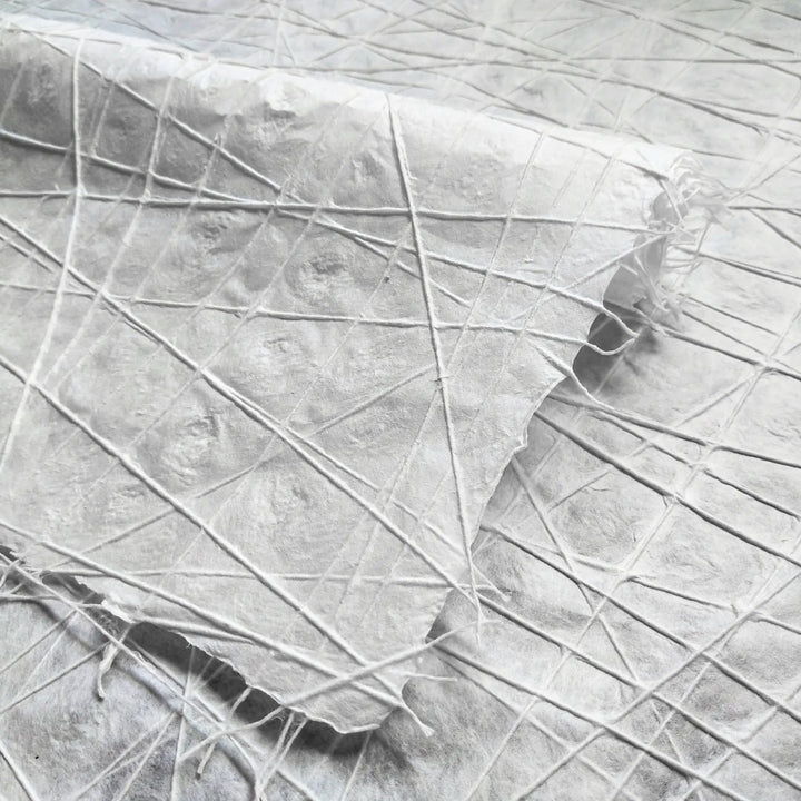 White handmade paper from Kozo Studio featuring interlaced cotton threads across mulberry pulp, showcasing an intricate, handcrafted texture with water dimpling details.