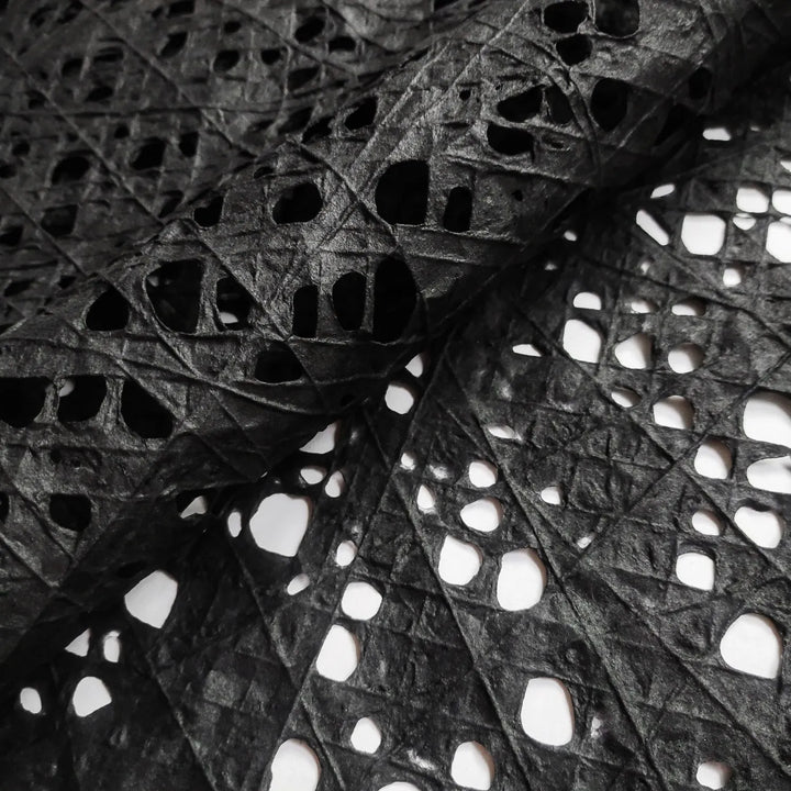 Black handmade mulberry paper featuring an intricate fishnet design created with cotton threads over kozo pulp, crafted by Kozo Studio for art and decor projects.
